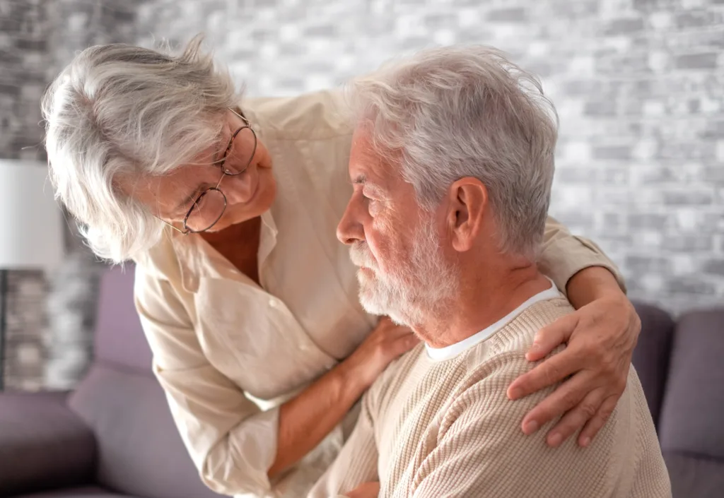 Old worried senior woman comforting her depressed, mental ill husband, unhappy elderly man at home need medical help.