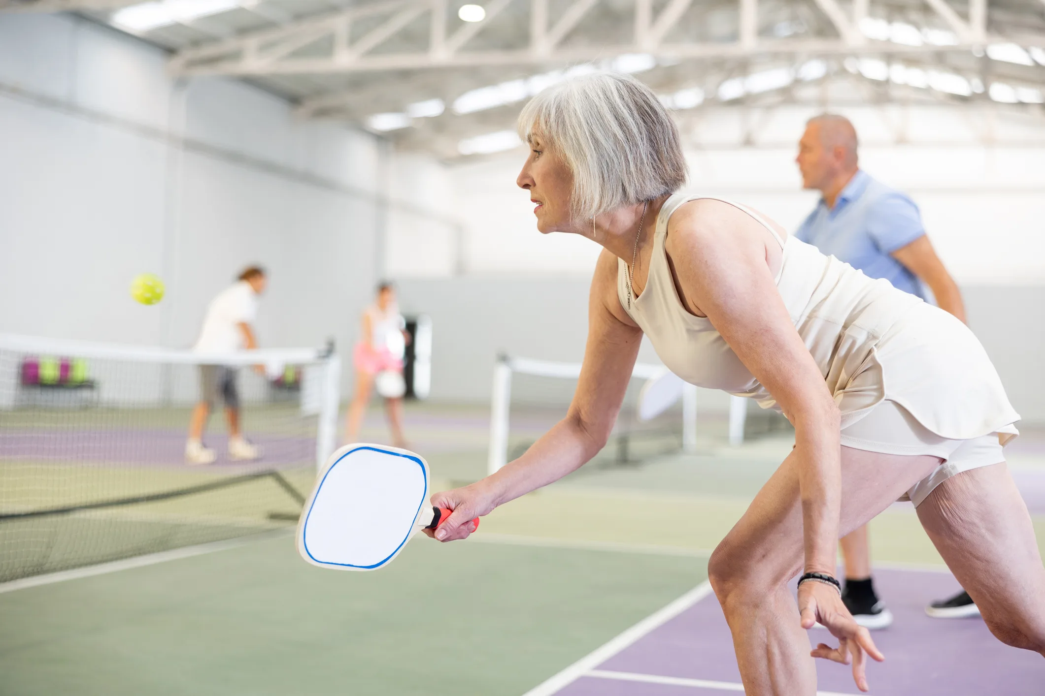 Mature woman playing doubles pickleball game, healthy lifestyle concept