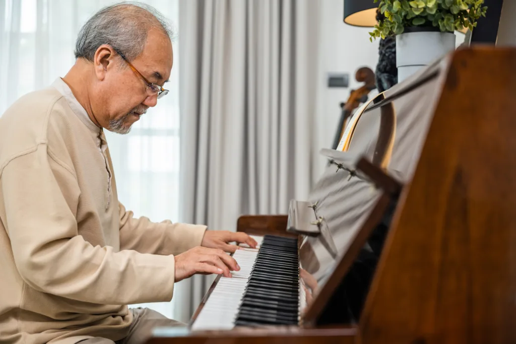 Asian senior retired man learning to play piano at home