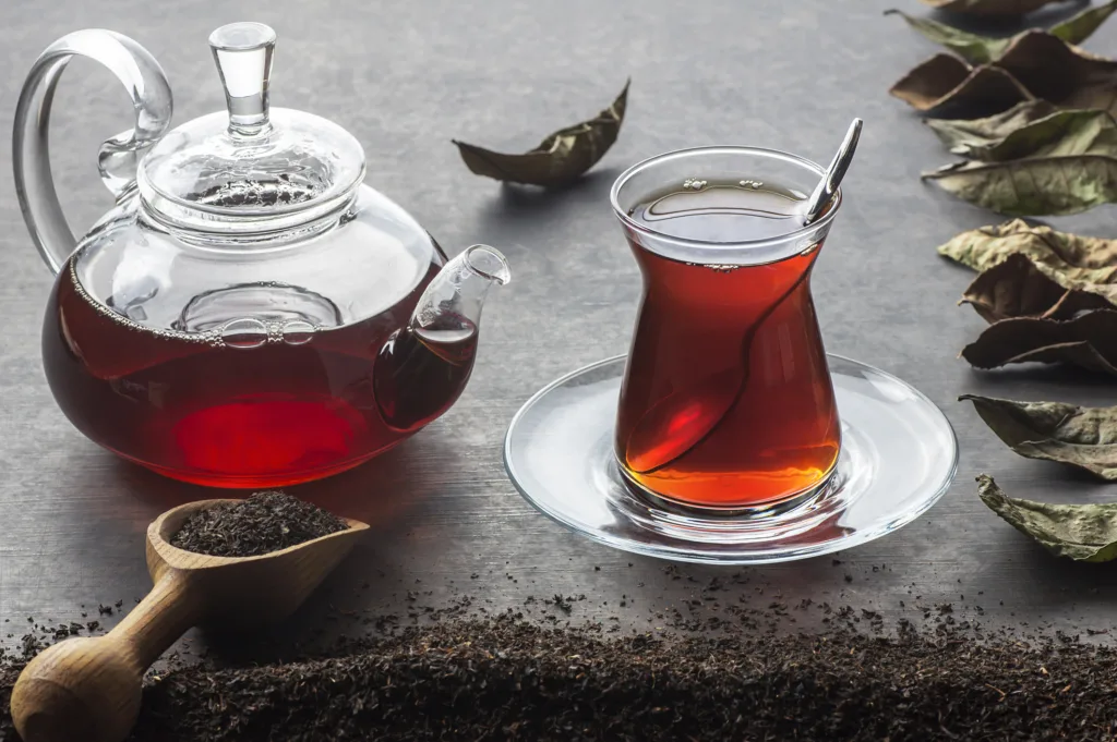 Glass Turkish brewed black tea and glass teapot with dry black tea and dried tea leaves on black rustic table