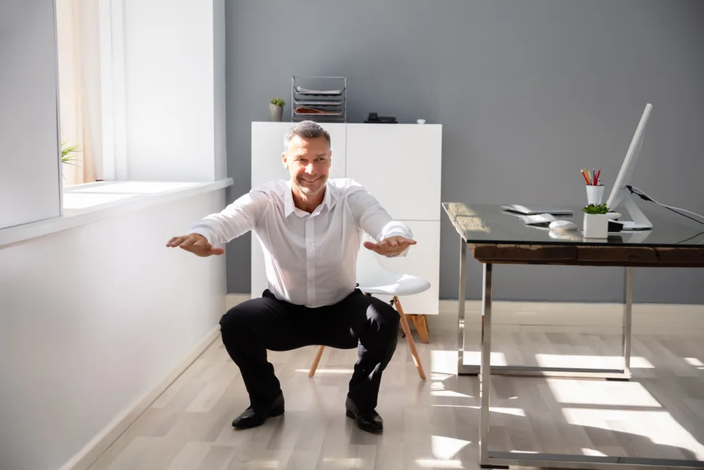 Businessman Doing Squats Exercise In Office