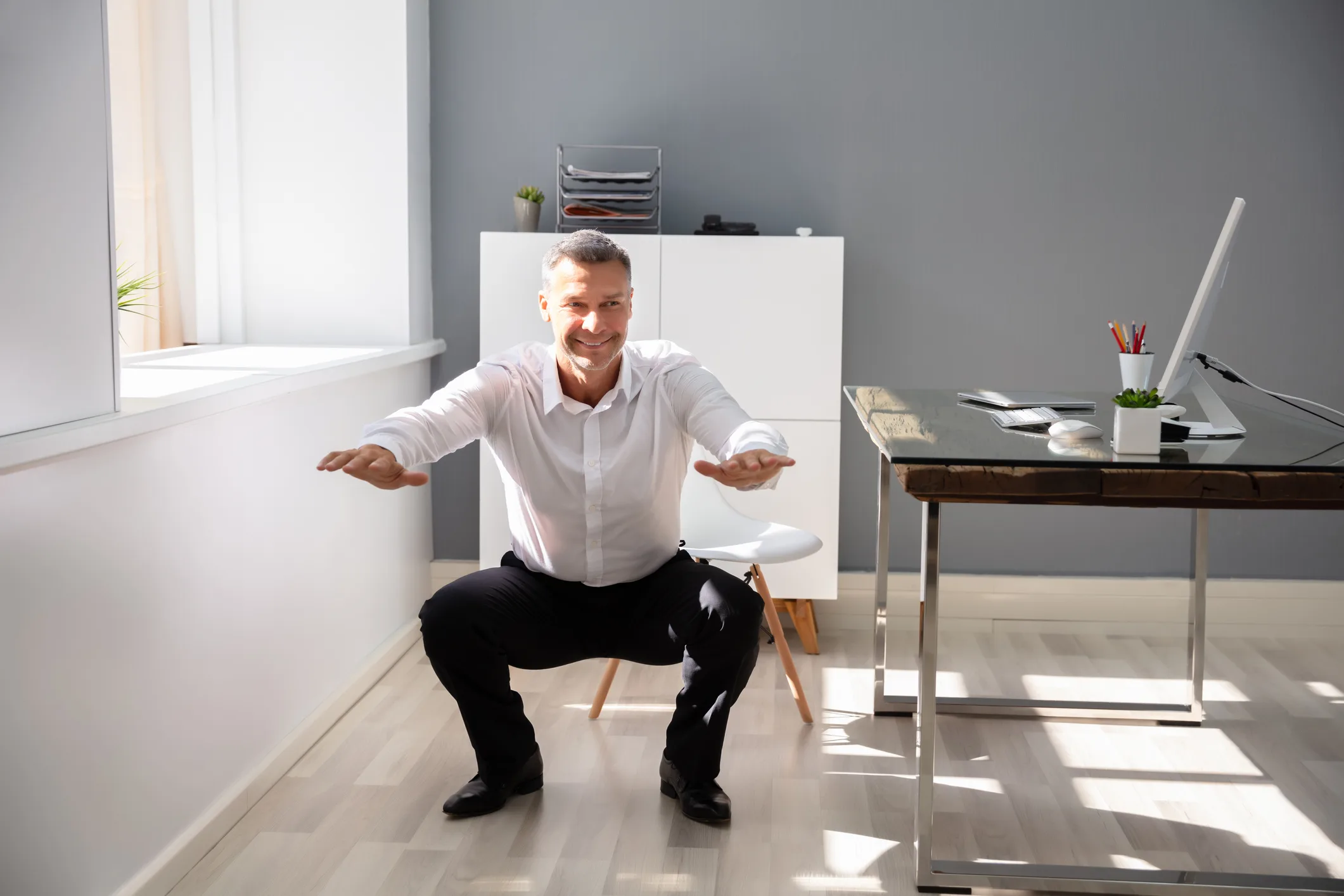 Businessman Doing Squats Exercise In Office