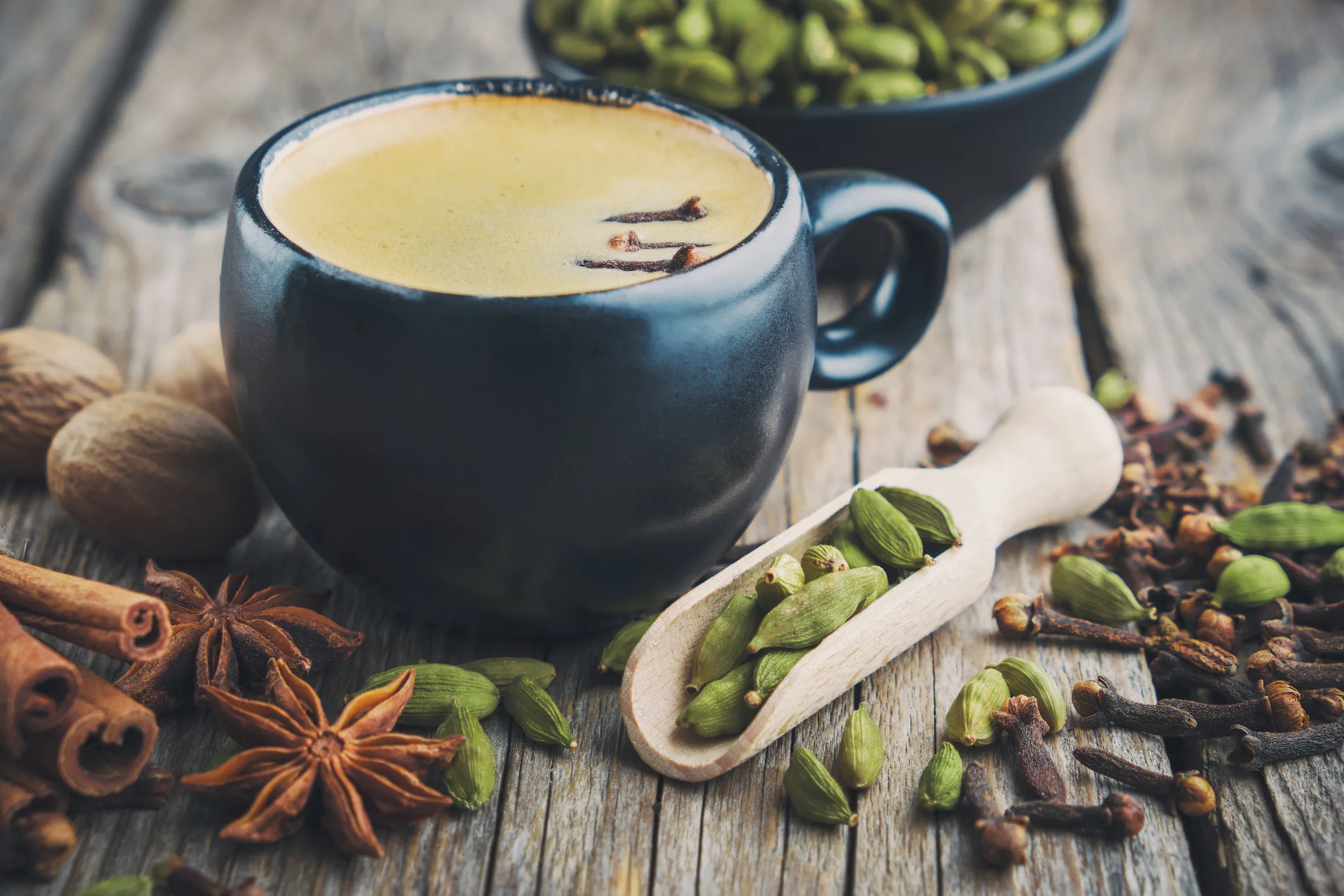 Cup of healthy ayurvedic masala tea or coffee with aromatic spices. Cinnamon sticks, cardamom, allspices and anise on wooden table.