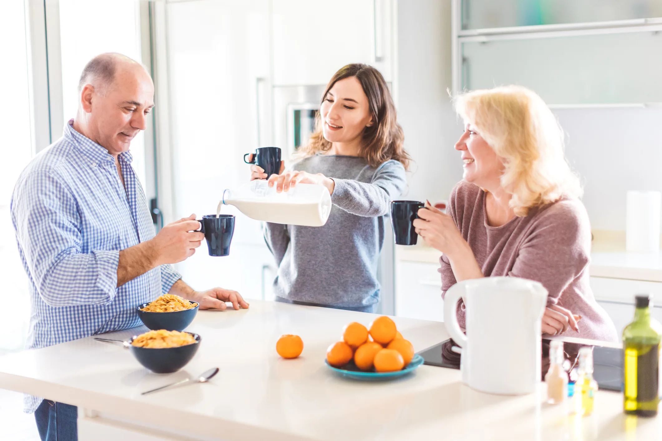Happy multiracial family having breakfast in the kitchen - daughter pouring the milk into her father's mug