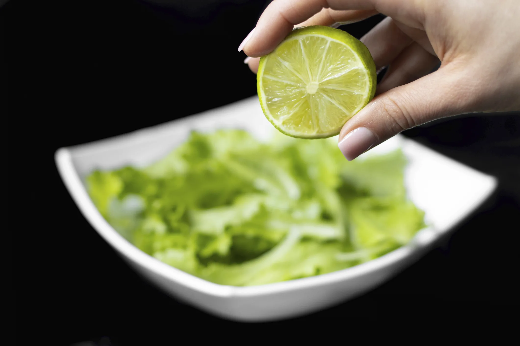 Hand squeezing half of a fresh lime on a black background.