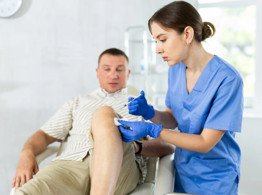 Female doctor performs intra-articular injection treatment of knee bursitis to man patient
