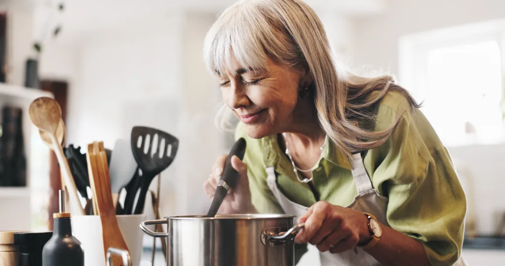 Aroma, cooking and mature woman in kitchen in home with smelling dinner, meal or dish. Happy, pot and female person with satisfaction for scent of supper with health, wellness and nutrition in house.