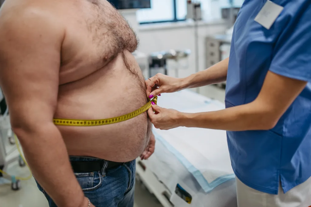 Female doctor measuring waist of overweight patient using tape measure. Obesity affecting middle-aged men's health. Concept of health risks of overwight and obesity.