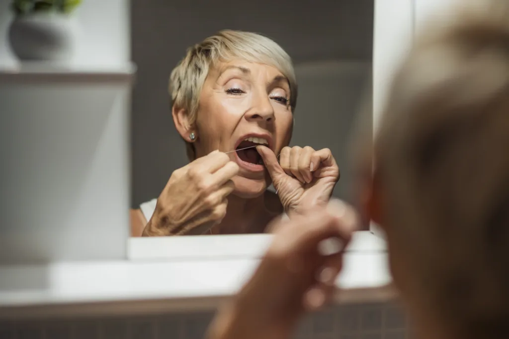 Middle aged woman flossing in front of mirror