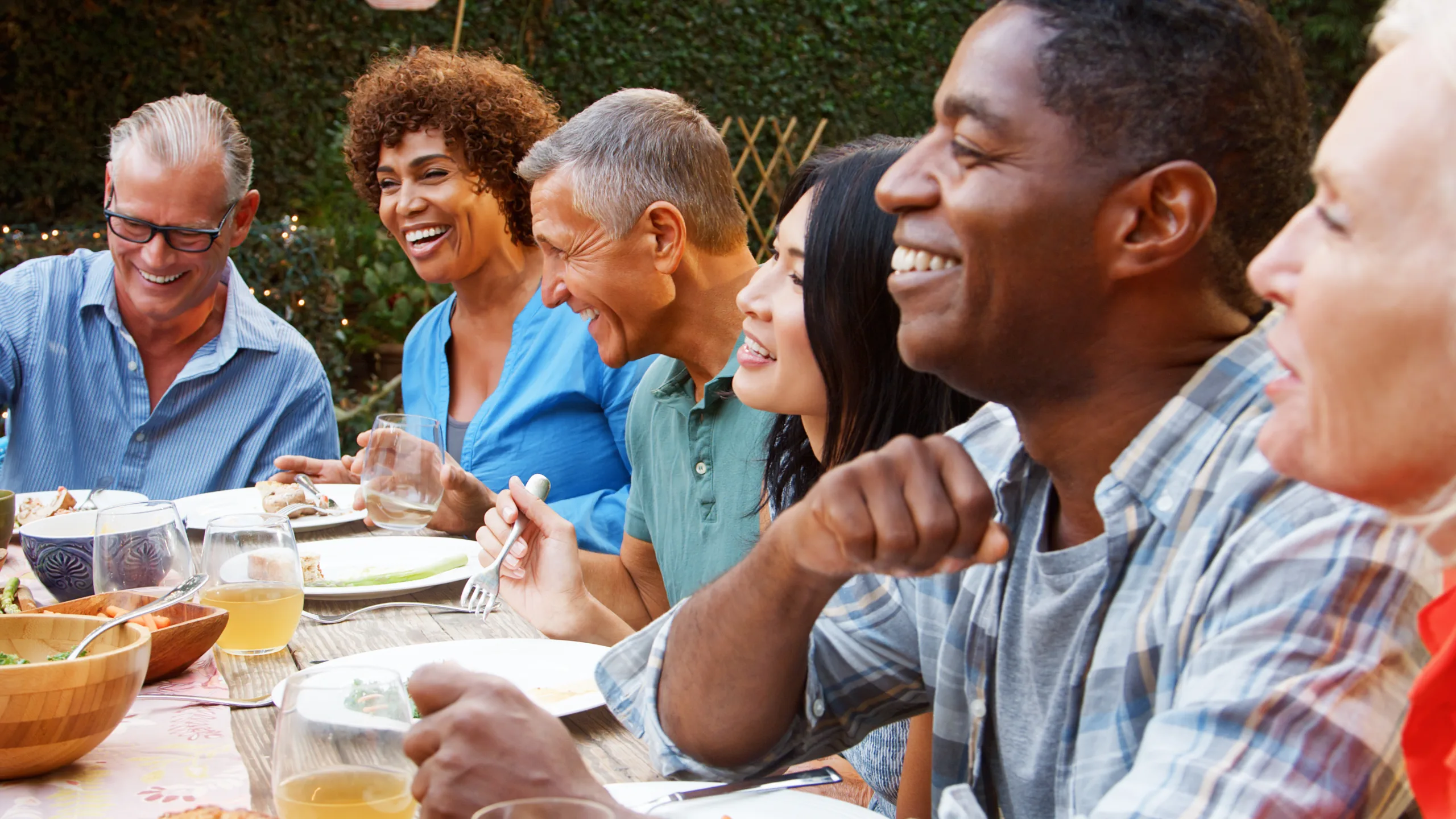Group Of Mature Friends Sitting Around Table Enjoying Outdoor Meal In Backyard