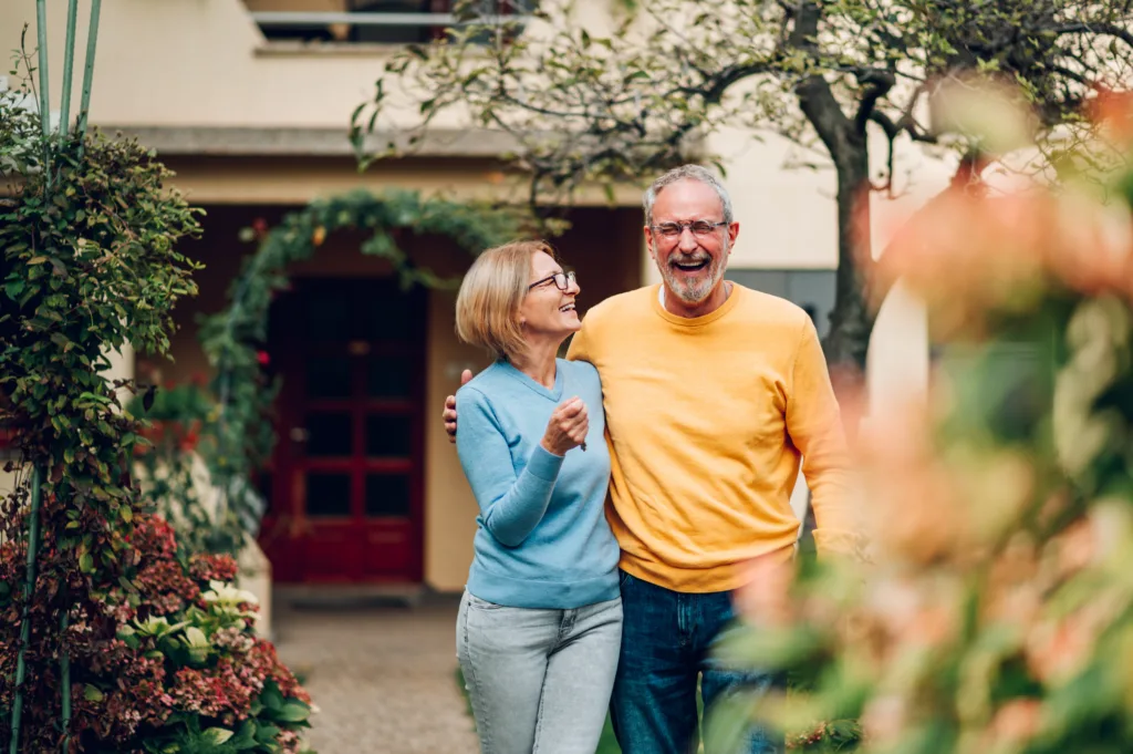 Senior couple holding keys and standing outside their new home