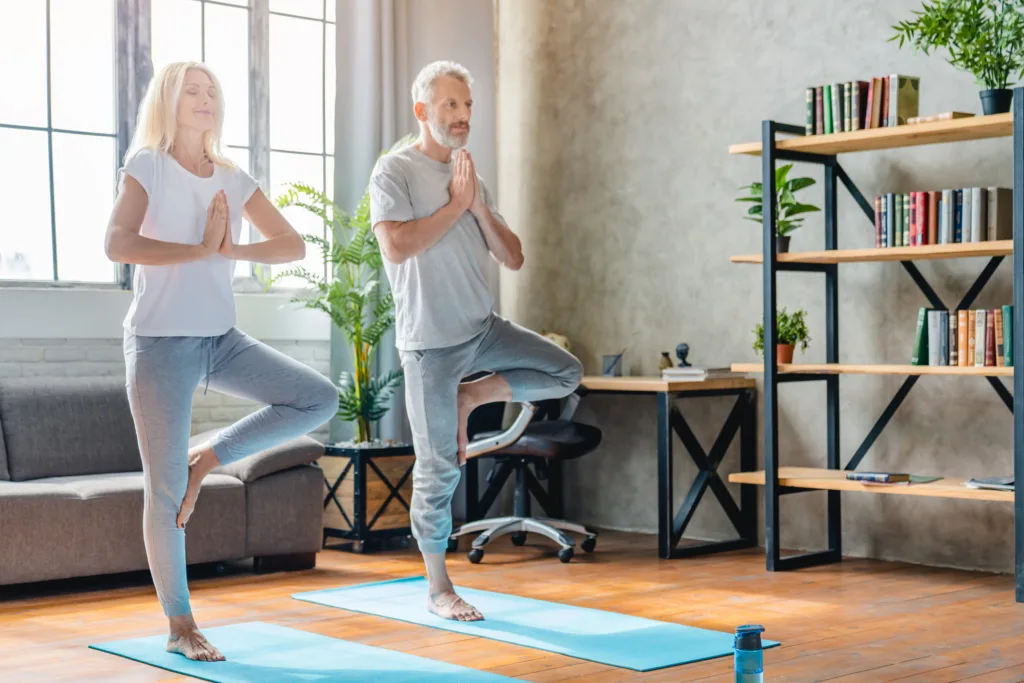 Senior couple performing tree pose on yoga mats at home while practicing