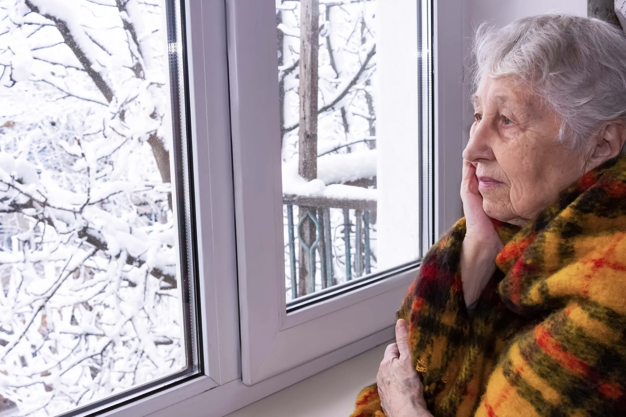 Old lonely woman sitting near the window in his house.
