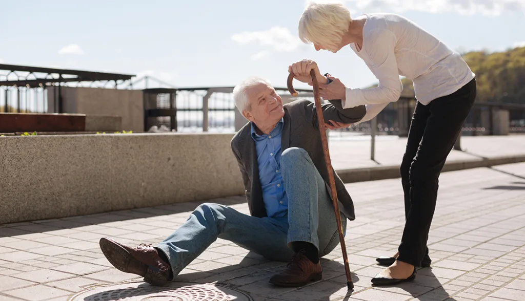 Older man being helped off ground by older woman