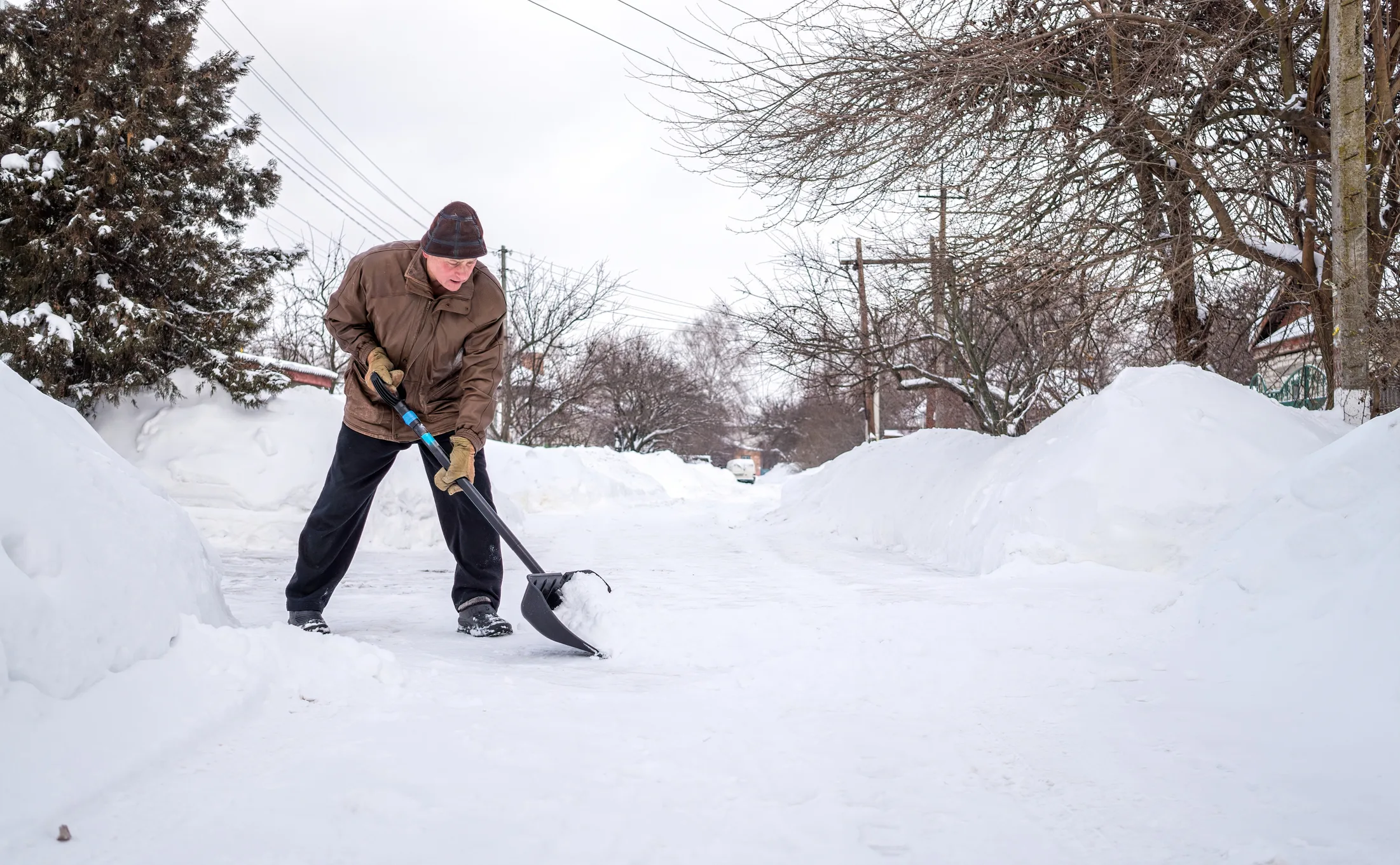 elderly man with a shovel in his hands clears the street after a heavy snowfall. Man at seasonal work
