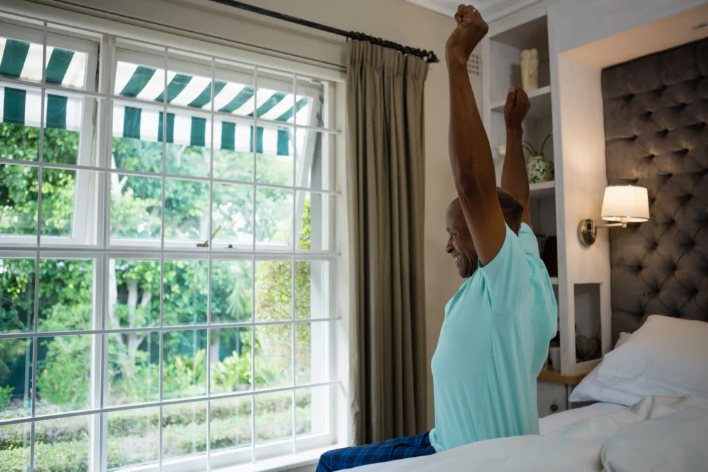 Side view senior man stretching arms while sitting on bed