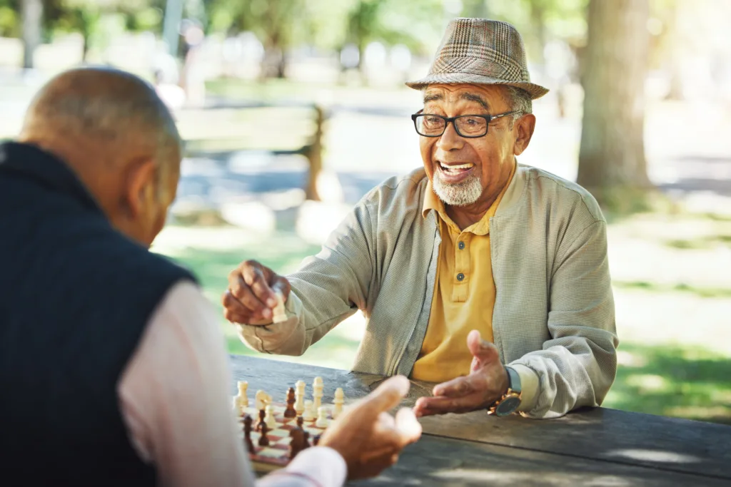 Elderly men in park, chess game and winner of competition or challenge, friends in retirement and happiness. Achievement, success and contest outdoor, moving piece for checkmate and problem solving