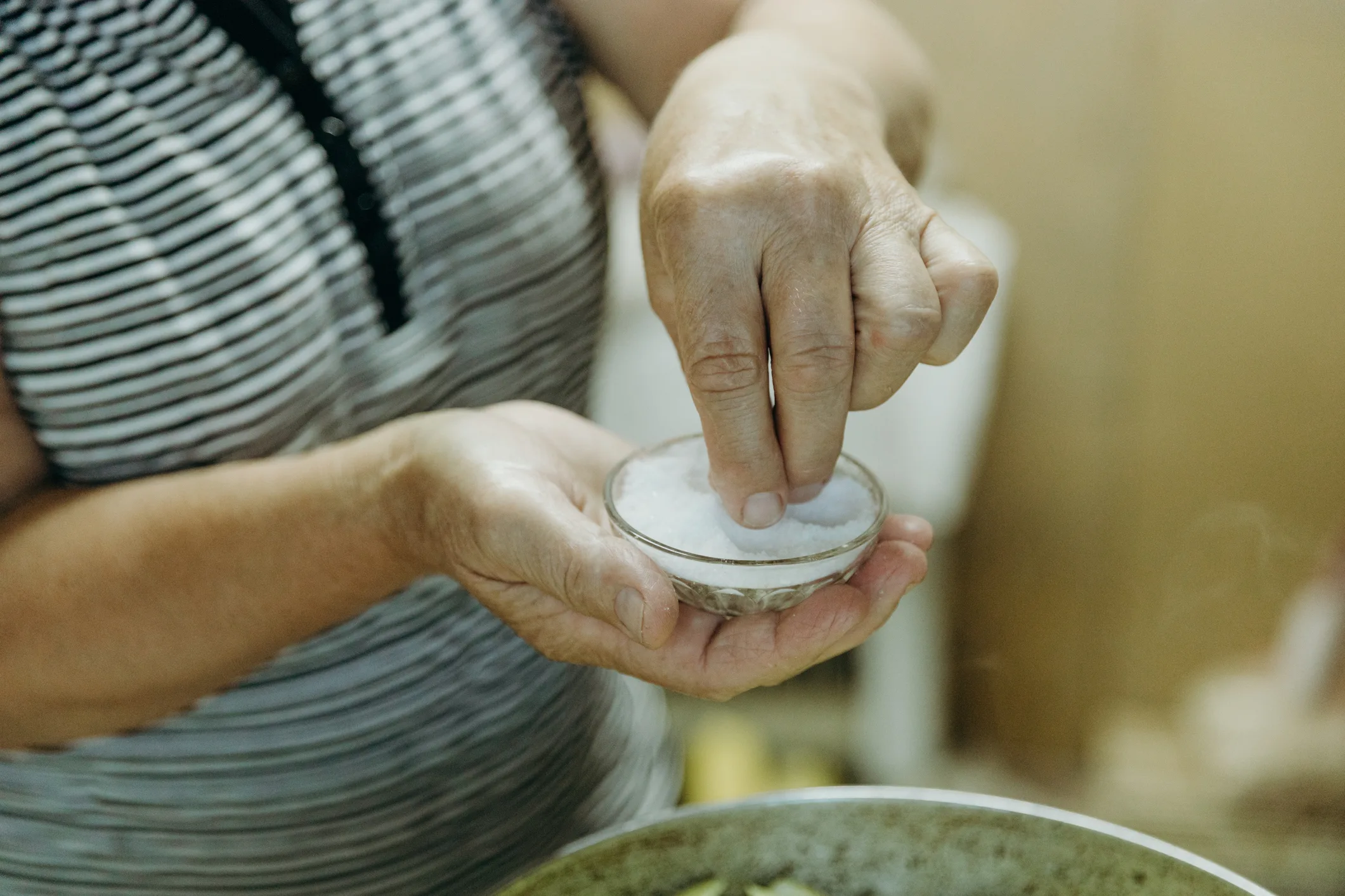 An elderly woman is frying potatoes in a frying pan on the stove.