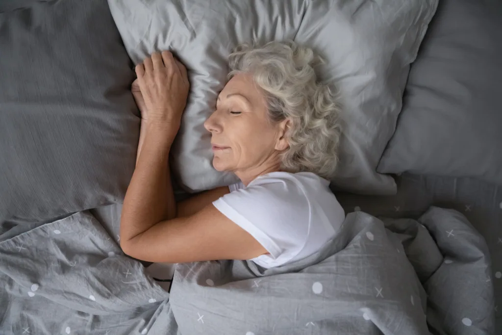 Happy mature woman sleeping on soft pillow under blanket.