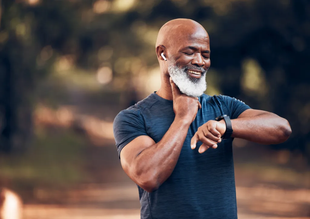 Fitness, black man and watch for pulse time and exercise while listening to music outdoor. Senior person with happy smartwatch for performance in forest with training workout for health and wellness
