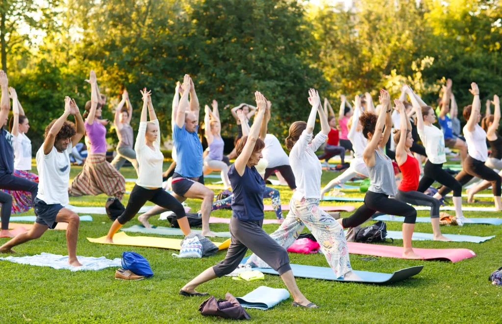 big group of adults attending a yoga class outside in park