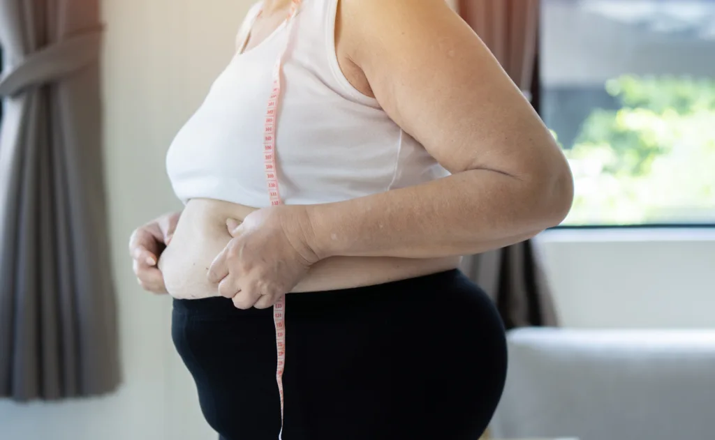 Fat woman, fat belly, chubby, obese woman hand holding excessive belly fat with measure tape,