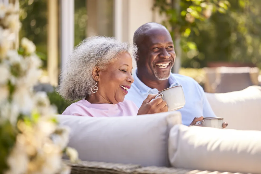 Retired Couple Sitting Outdoors At Home Having Morning Coffee Together