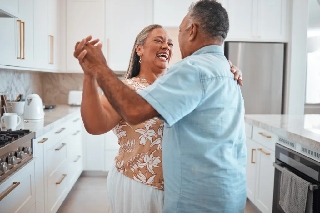 Happy senior couple, dance and laughing in joyful happiness for relationship bonding in the kitchen at home. Elderly man and woman with smile dancing together for romantic moment in love and care