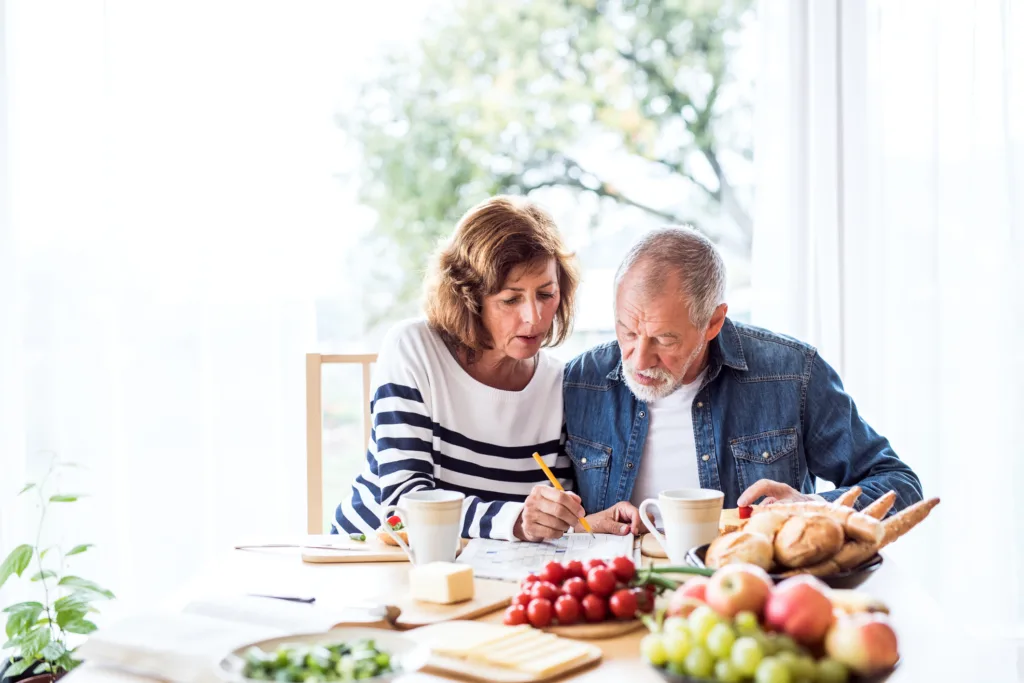 Senior couple eating breakfast at home while doing a crossword puzzle