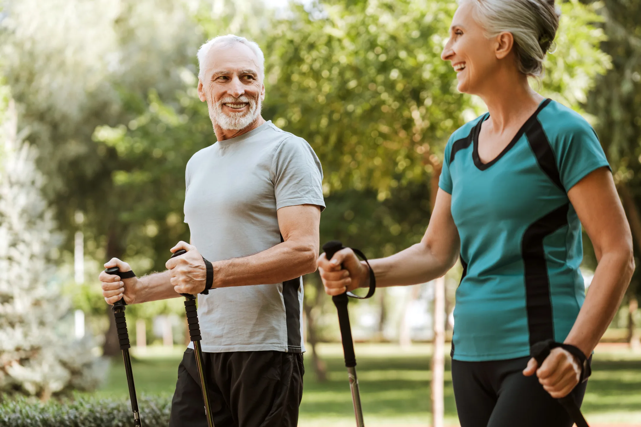 Smiling, attractive senior couple practicing nordic walking using trekking poles in park