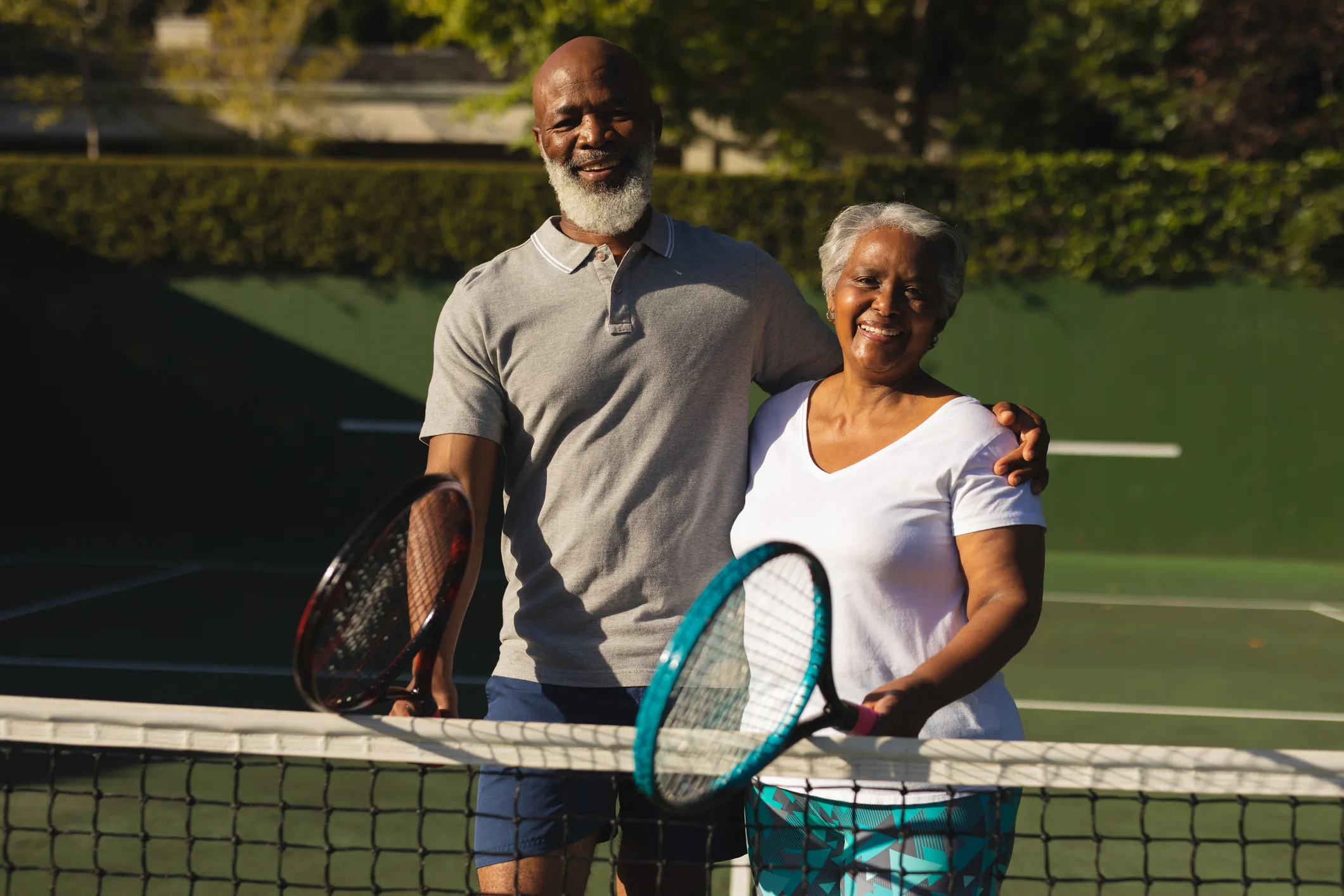 Portrait of smiling senior african american couple with tennis rackets on tennis court