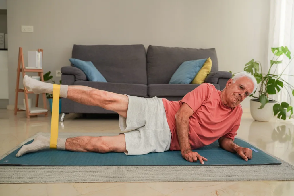 Senior man doing leg exercises with resistance band on yoga mat at home