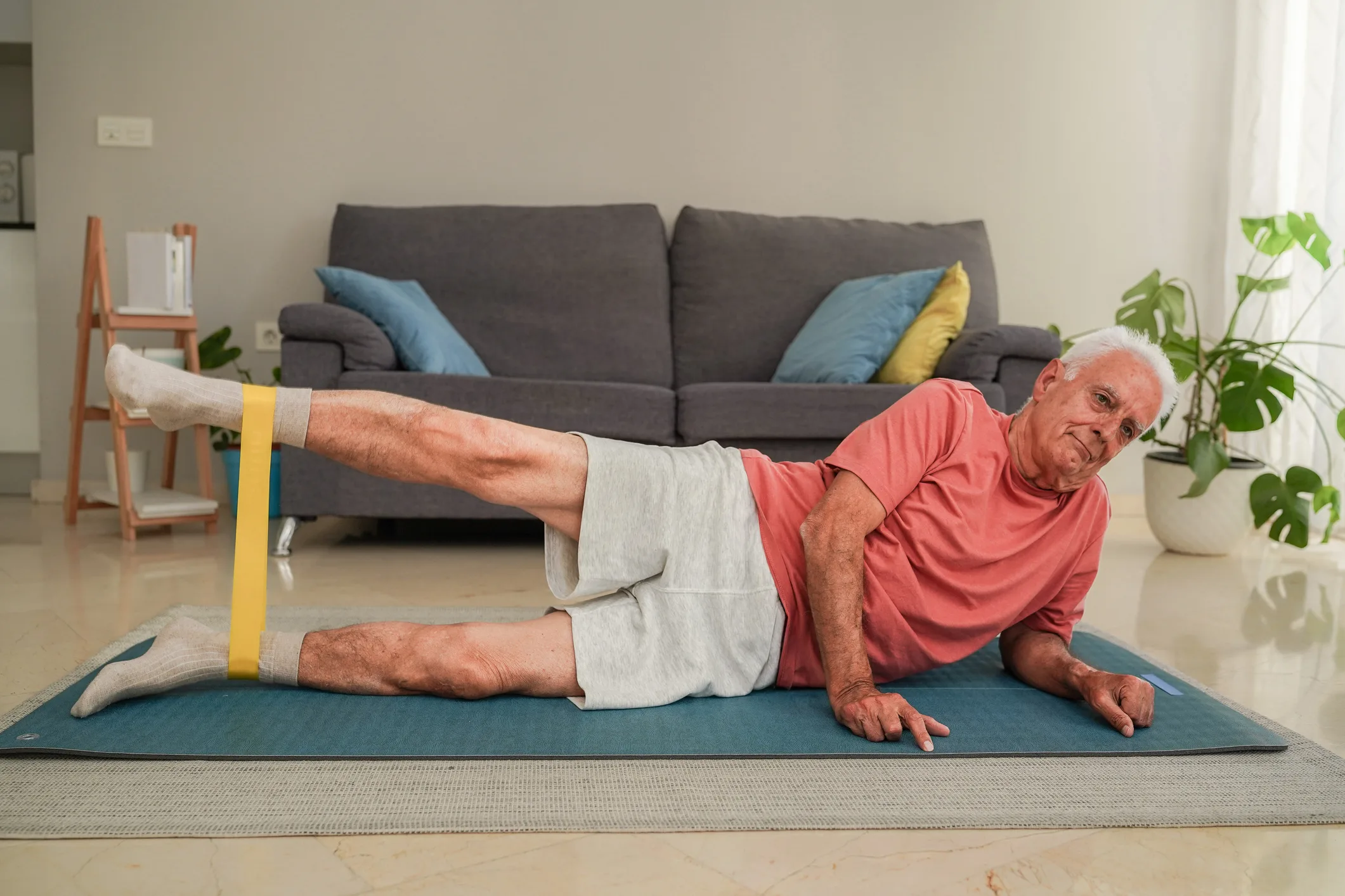 Senior man doing leg exercises with resistance band on yoga mat at home
