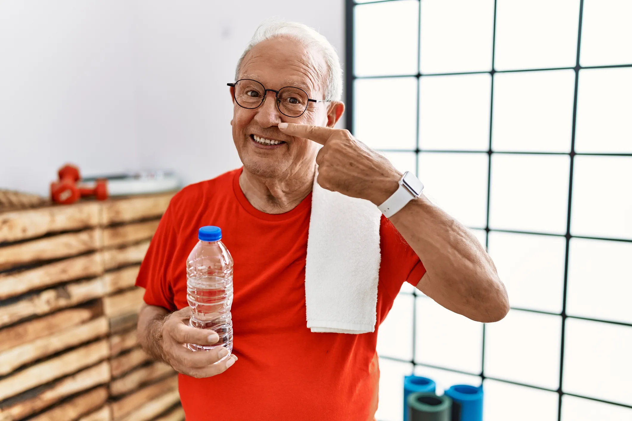 Senior man wearing sportswear and towel at the gym pointing with hand finger to face and nose, smiling cheerful. beauty concept