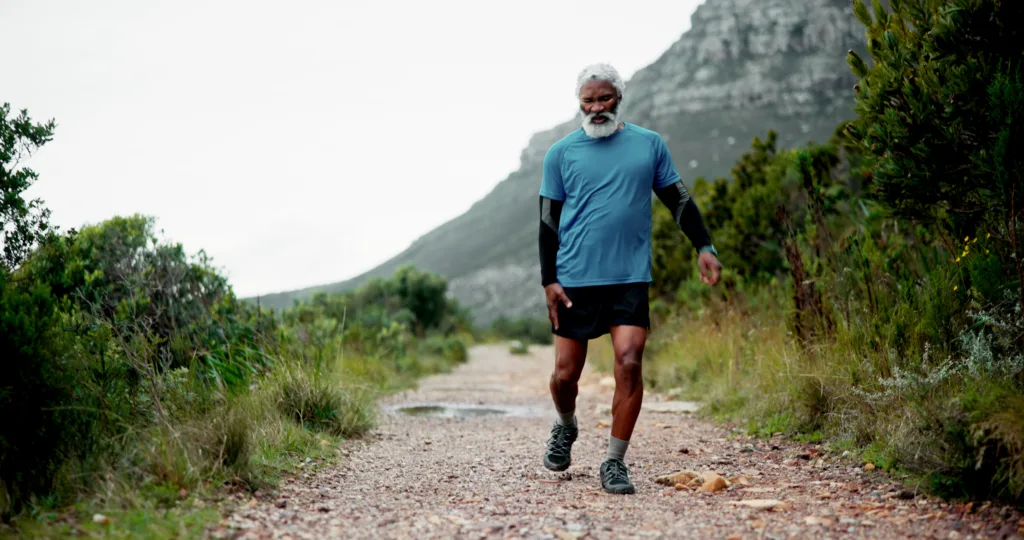 Hip pain, senior black man and injury in nature for fitness, workout or training with accident. Runner, dead leg and elderly sports person on trail hurt with tendinitis, inflammation and arthritis