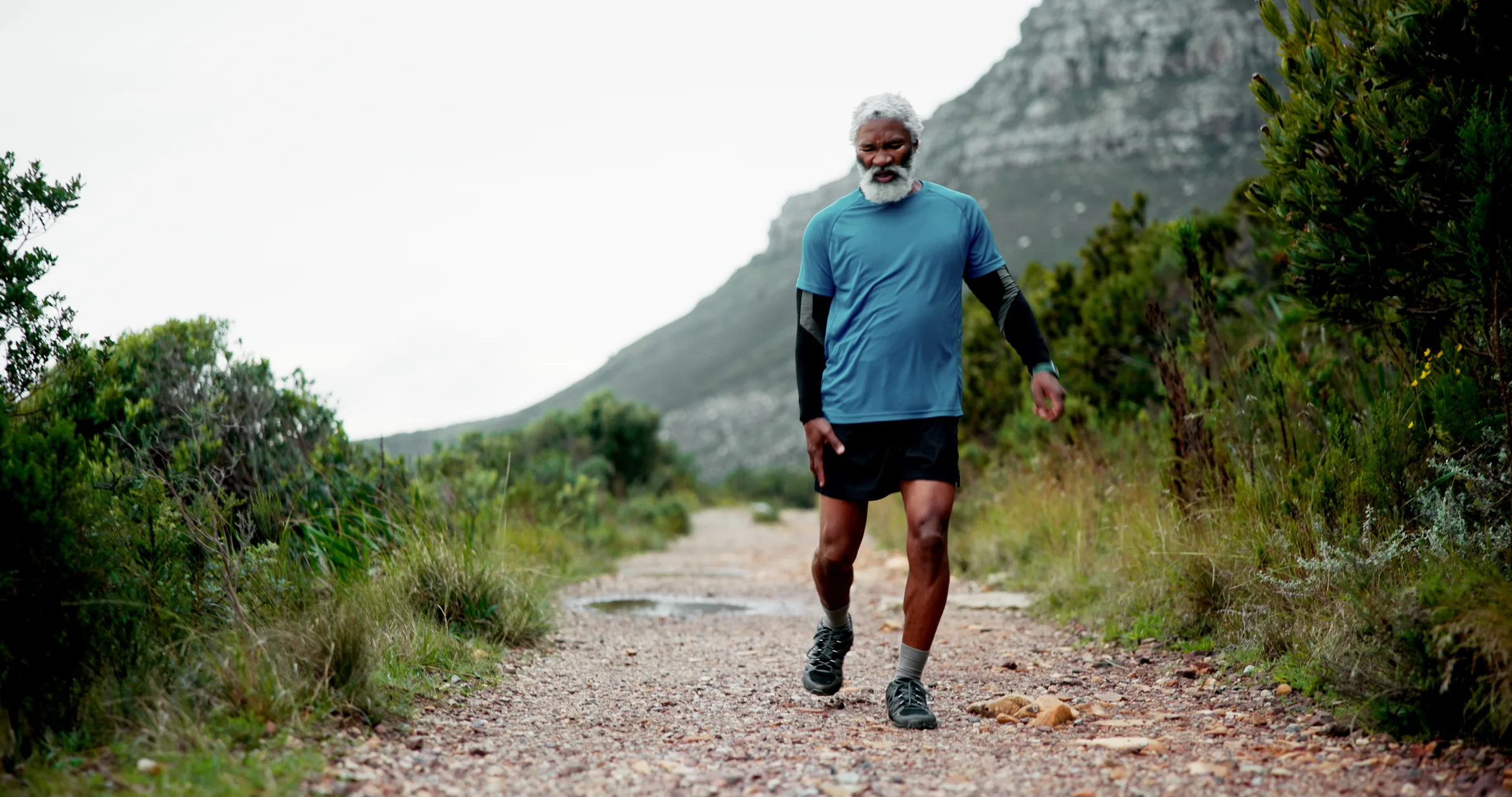 Hip pain, senior black man and injury in nature for fitness, workout or training with accident. Runner, dead leg and elderly sports person on trail hurt with tendinitis, inflammation and arthritis