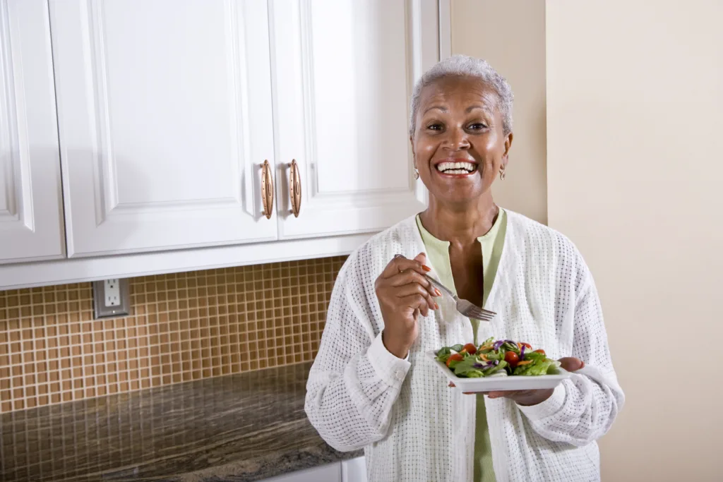 Mature African American woman eating salad in kitchen