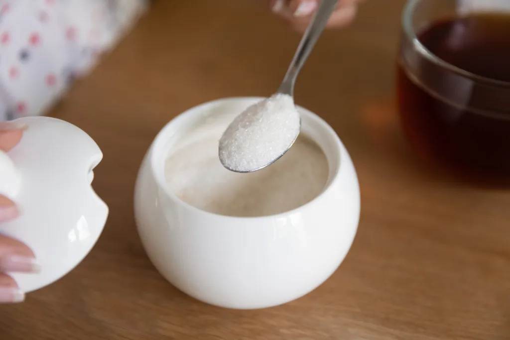 Close up woman putting spoon of sugar in black tea