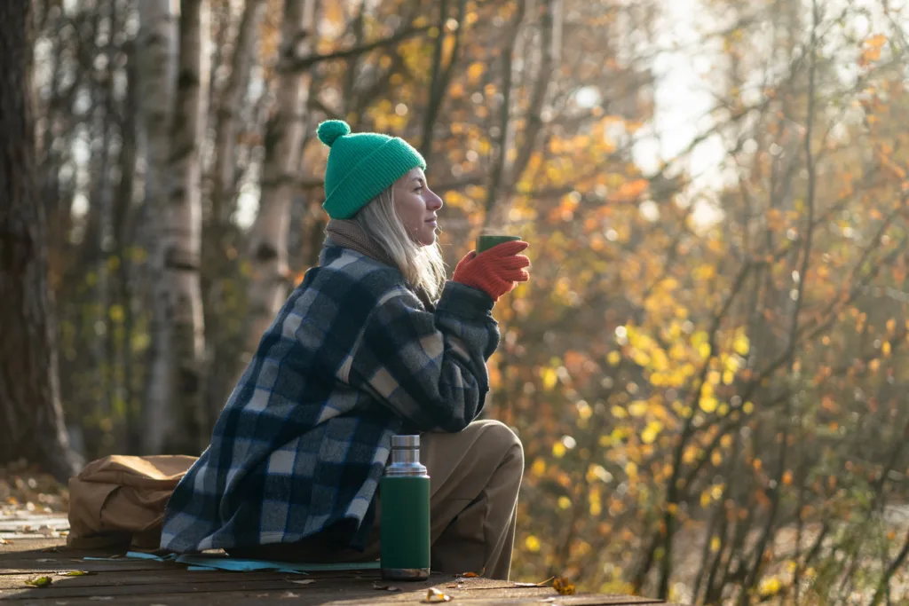 Tranquil meditative woman enjoys hot tea, sunny nature on eco trail in fall forest. Responsible life
