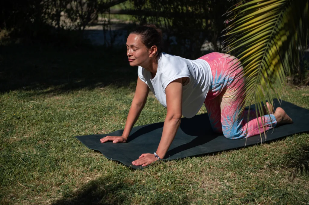Woman practicing yoga outdoors in garden on a sunny day, performing cat-cow stretch on yoga mat